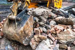 close-up of excavator bucket loading rocks, stones, earth and concrete bricks